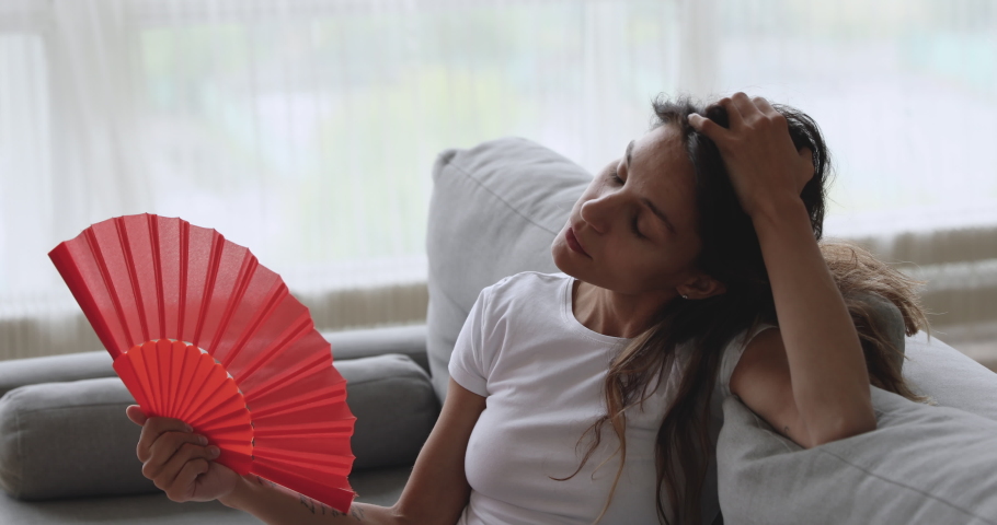 Overheated unhappy young woman feeling hot waving fan annoyed with high temperature sit on couch at home, stressed sweaty girl sweating suffer from summer weather heat problem without air conditioner Royalty-Free Stock Footage #1032911132