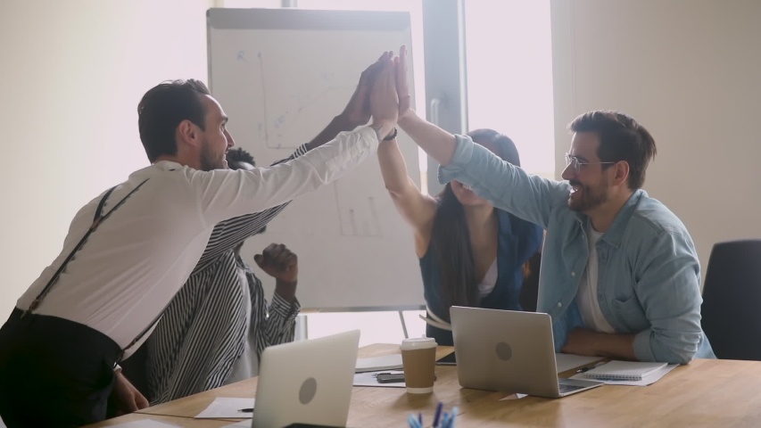Happy successful multiethnic business team give high five sit at table, motivated diverse executives group engaged in teambuilding celebrate good teamwork result achieved corporate goals concept Royalty-Free Stock Footage #1032911195