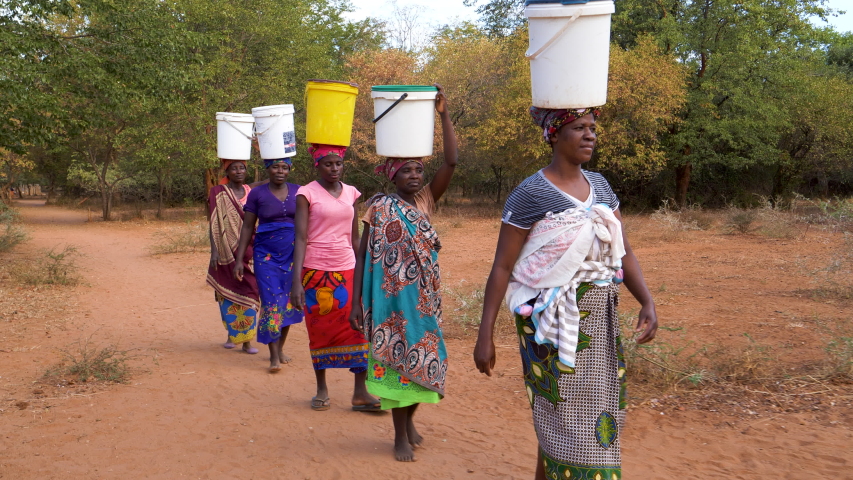 Poverty.Inequality.Poor people in Africa unable to maintain social distance due to water crisis. Five woman make the long journey home carry water in plastic containers on their heads  Royalty-Free Stock Footage #1032916136