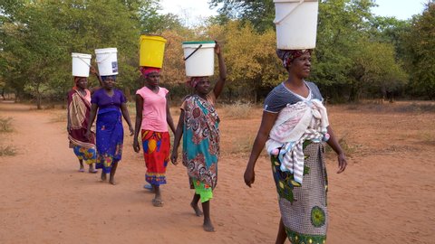 Poverty.Inequality.Poor people in Africa unable to maintain social distance due to water crisis. Five woman make the long journey home carry water in plastic containers on their heads 