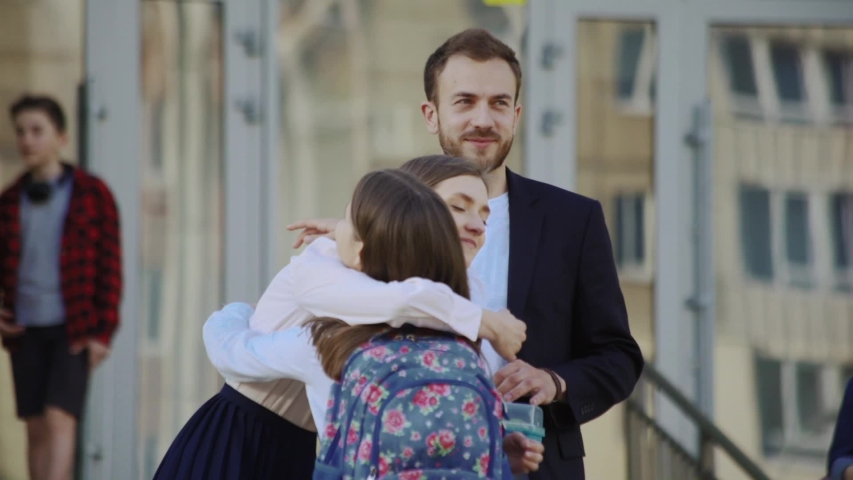 Happy smiling parents leading their cute daughter to school hugging together in the school courtyard. First day of studies. Royalty-Free Stock Footage #1032918215