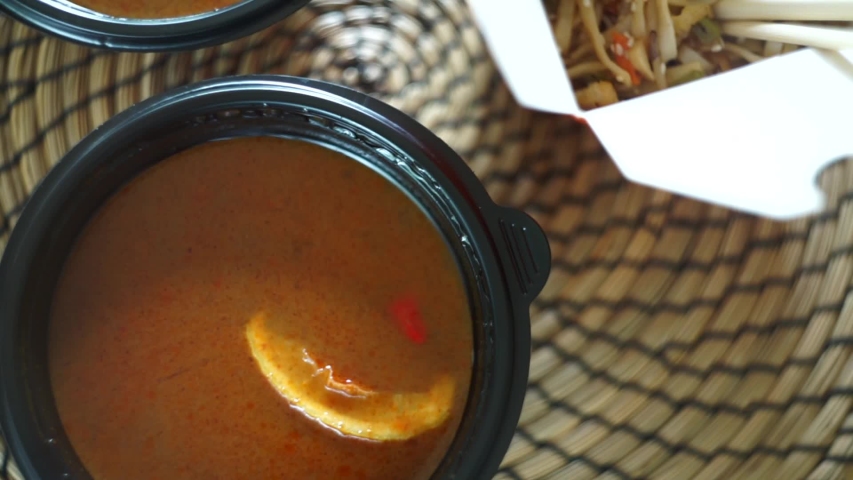Close up asian food on bamboo table. Tom yam soup in plate - traditional spicy Thai delicious with lemongrass, seafood, galangal and coconut milk. Noodles and rice