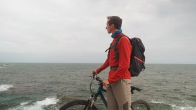 Active summer sports: young man cyclist with mountain bike standing enjoying colorful sea view. Active people colorful video. Bike riding in summer, healthy people outdoors. Bicycle sport man