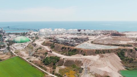 Aerial footage over the island coastline with industry factory on the seashore. View from drone of the fuel gas power plant with industrial waste on the hills. Pollution in nature on industrial isle.