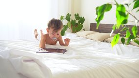 Little boy looks into tablet lying in bed