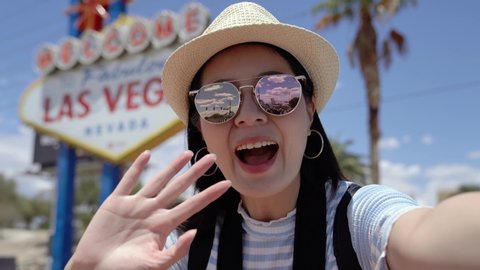 young asian college girl student study abroad in usa. female teenager talking on video phone call with family while standing by Las Vegas Welcome sign. woman presenting and inviting to come to camera