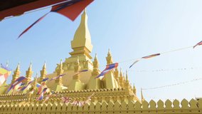 (Selective focus) Slow motion video of Laos flags waving in the foreground with the beautiful Pha That Luang in the background. Pha That Luang is a gold-covered large Buddhist stupa in Vientiane, Laos
