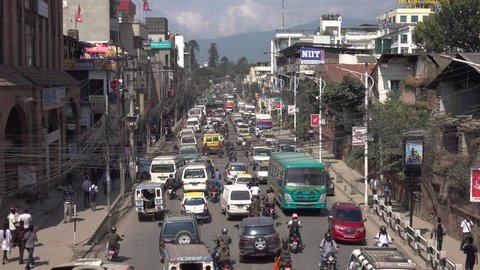 KATHMANDU, NEPAL - SEPTEMBER 2018: Stunning view from above of chaotic daytime traffic in the capital city of Nepal. Cars and motorbike riders get stuck on the asphalt road running through Kathmandu.