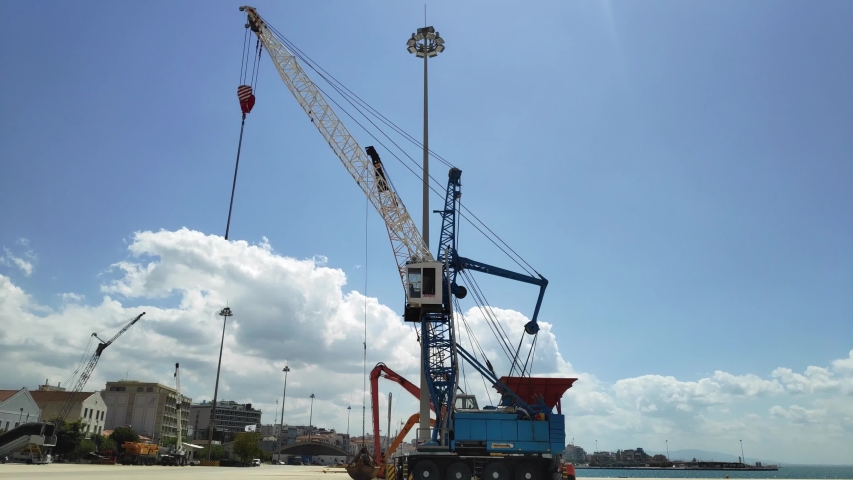 A large crane at the port for loading heavy cargo on the ships or placing sailor boats into the sea water. Time lapse shot.