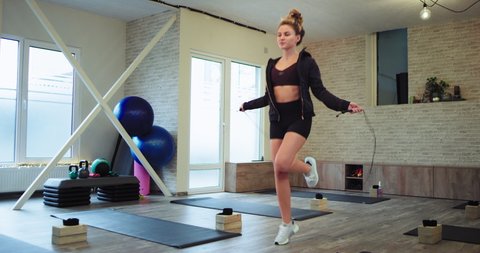 Stylish sporty woman with a fi muscle body jumping on a rope in a large spacious aerobic studio very concentrated in a good mood she practicing the sport
