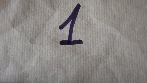 hand writes the number one 1 on wrapping paper employing a black felt tip pen