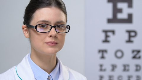 Professional female optician looking at camera against eye chart background