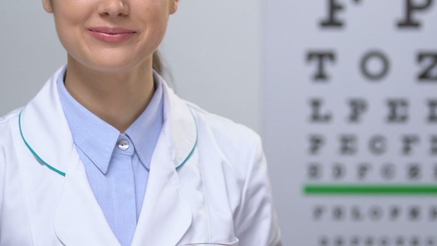 Smiling female doctor showing carrot juice against eye chart background, health Royalty-Free Stock Footage #1032951437