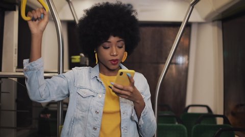 Happy afro businesswoman cheering celebrating looking at smartphone. Young urban professional successful business woman receiving good news riding in public transport.