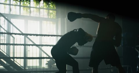 Cinematic slow motion shot of two professional young muscular shirtless male boxers are fighting and embracing after in a boxing ring.