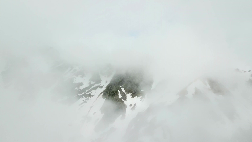 Aerial, tilt down, drone shot, over clouds, revealing snowy mountain tops, of Chamonix Mont-Blanc, on a moody and foggy day, near Aiguille Du Midi , in the French alps, in Haute-Savoie, France
