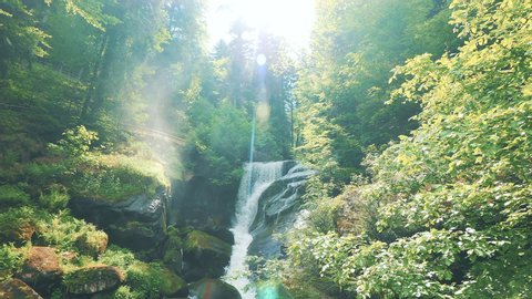 View of a beautiful waterfall and the cloud of tiny water drops under the sun rays and lens flares. Camera panningement. Gimbal shot