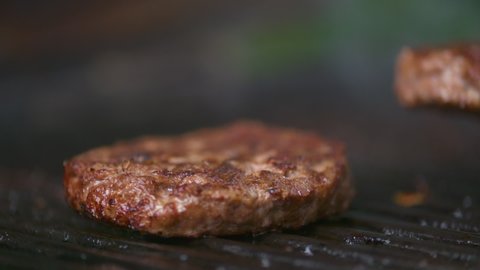 Slow motion close-up, rotating juicy, mouthwatering beef burgers on a flaming grill