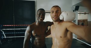 Slow motion of two professional young muscular shirtless male boxers of different ethnicities are making a selfie after friendly fighting in a boxing ring.