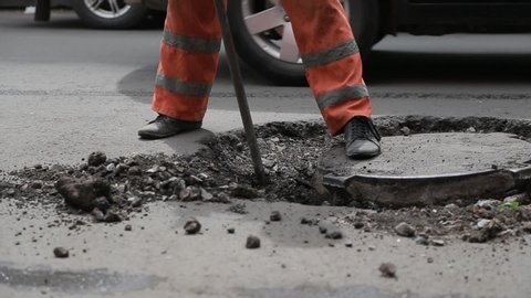 Road worker with steel bar on road maintenance service. Cleaning sewer hatch pavement with steel rod to construct new highway. Asphalt mending job with demolition steel bar on urban city street track.