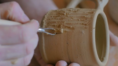 Professional potter making pattern on clay mug with special tool in pottery workshop, studio. Crafting, artwork and handmade concept Stock Video