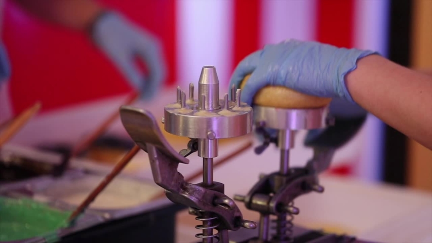 woman hands in blue sterile gloves make holes in donuts using special equipment. extreme slow motion. close view