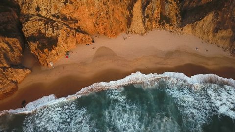 Top down view of waves breaking in the sand in Ursa Beach, Sintra, Portugal. A person running along the beach at sunset