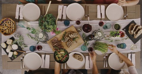 Friends having a dinner party together, top down view of dinner table with six friends serving food and making dinner plates