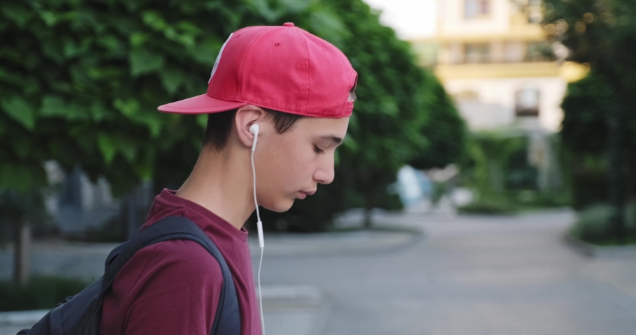 Teenager walking on the street and  listen to the music in earphones. 