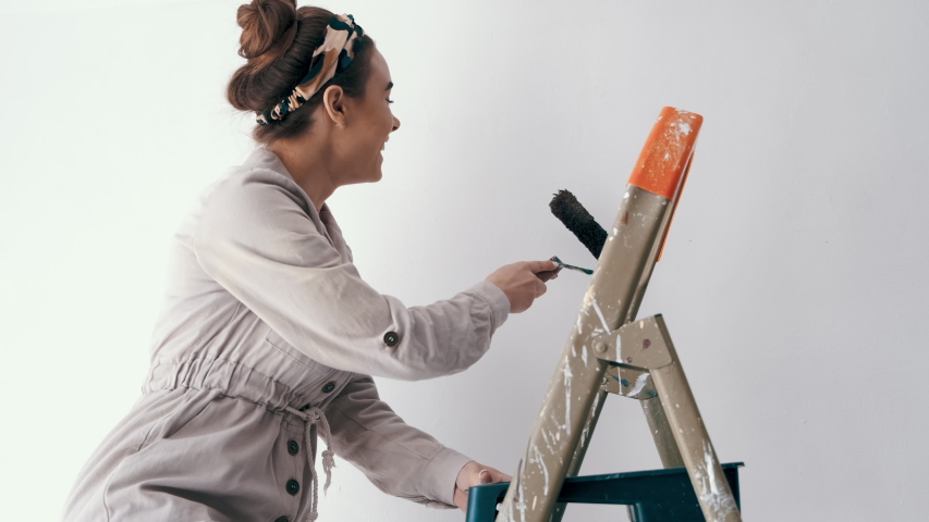 wife standing on a ladder while her husband paints the wall and helps her