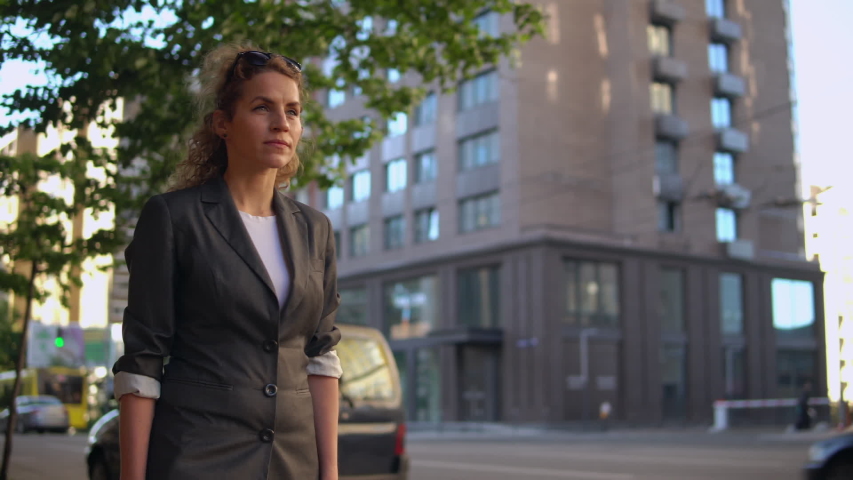 Adult beautiful woman walking on the street in early morning. caucasian businesswoman wearing elegant jacket going to work | Shutterstock HD Video #1033001384
