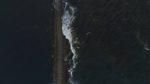 90 degree angle Aerial after Storm: Beautiful 4K Eastern Europe lighthouse pier - a bird eye view of Baltic Sea windy waves crashing against a walking path flooding it from above - Drone top view