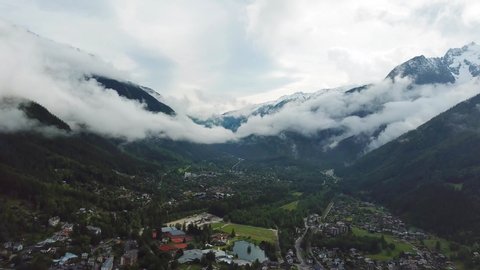 Aerial, reverse, drone shot, of foggy mountains and the Chamonix town, on a moody and cloudy, summer day, in the French alps, Haute-Savoie, France
