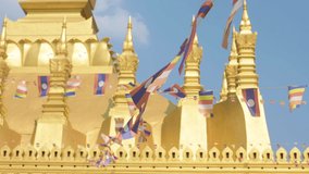 (Selective focus) Video of Laos flags waving in the foreground with the beautiful Pha That Luang in the background. Pha That Luang is a gold-covered large Buddhist stupa in Vientiane, Laos