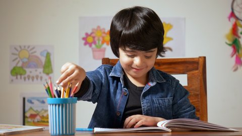 Talented Indian boy picking the color pencil to draw a picture - Education in Childhood. Little boy completing his art homework with the bight color shading pencil - child concept