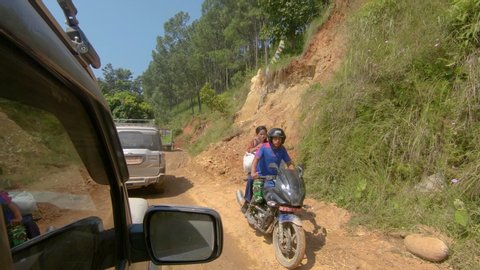 KATHMANDU, NEPAL - SEPTEMBER 2018: POV: Driving in a convoy of 4x4 jeeps transporting tourists across rural Nepal to Tibet. First person view of sitting inside a car driving along a bumpy dirt road.