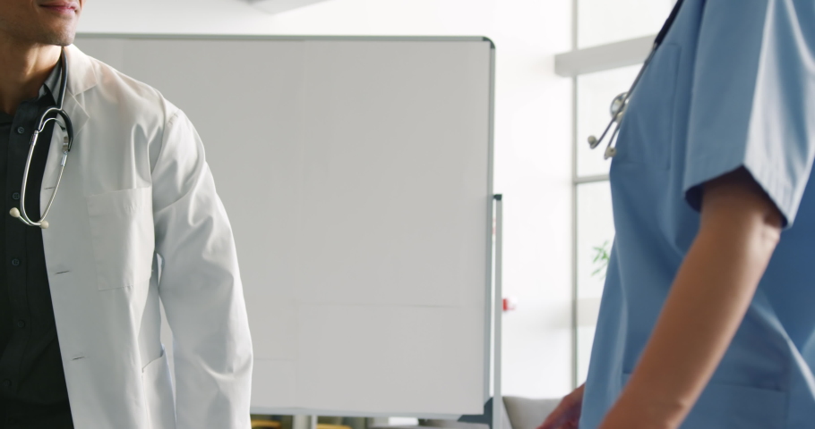 Slow motion tilt shot of a smiling young male and young female Caucasian doctors talking and shaking hands in hospital. Healthcare workers in the Coronavirus Covid19 pandemic