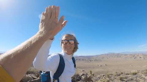 Couple of hikers reaches mountain top, celebrates with high five; Point of view of hiker man hand giving high five to partner; Two people enjoying outdoor sport activities in USA 