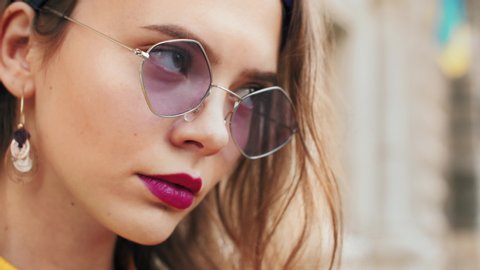 Young fashionable lady wearing trendy purple color sunglasses, colorful headband, posing outdoor, looking at camera. Close up portrait Stock Video