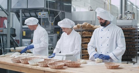 Professional bakers forming pieces of dough to baking bread on a big table in commercial kitchen industry