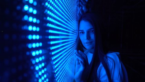 Millennial pretty girl near glowing bright colored LED SMD video wall with high saturated patterns
