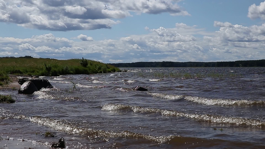 Cold north lake. Sandy beach and waves. Waves run onto the shore. Blue sky, clouds, lake
 with clean water.