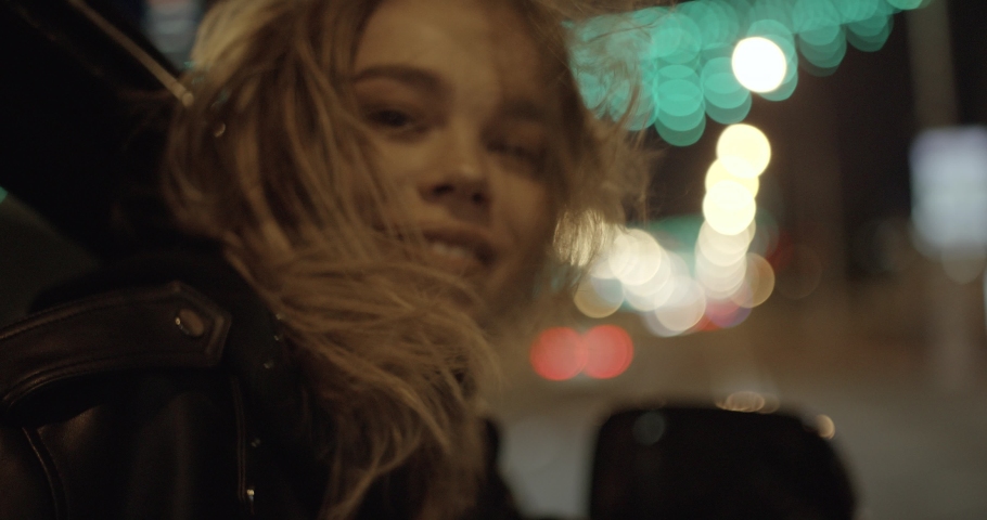 Young pretty girl in car, leans out passenger side car window, wind stirs her hair, she looks at the night city, night road, girl looking at the camera. | Shutterstock HD Video #1033025270