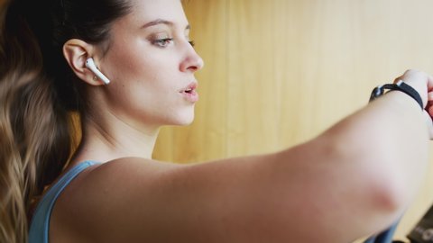 Woman Exercising On Treadmill At Home Wearing Wireless Earphones Checking Smart Watch