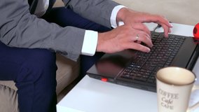 Hands of a businessman typing on a laptop computer indoors at home on a small table