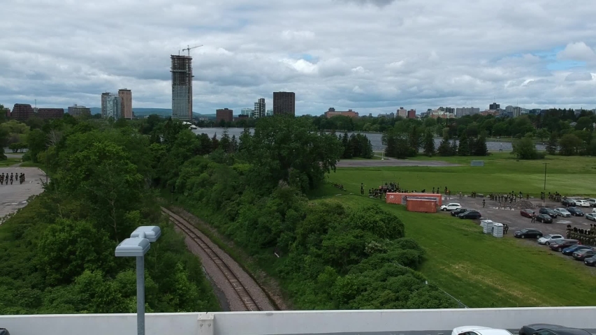 Drone footage over the edge of a parking garage revealing a train track through a forested area in Ottawa, Ontario.