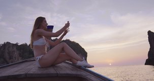 Girl tourist taking photo or video of sunset with smartphone on long tail boat tour. Phi Phi islands Asian summer holiday travel vacation adventure. Slow motion, hand held, shot on red. 
