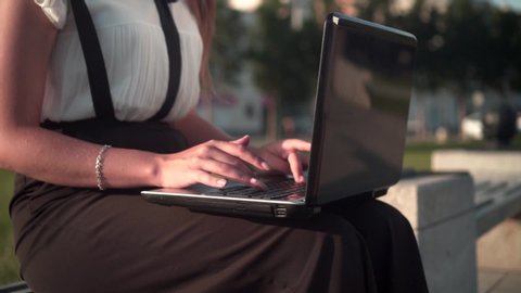 Caucasian young business woman in white shirt and glasses sits on a bench on the street and works on a laptop. The girl is unpleasantly surprised, she made a mistake.