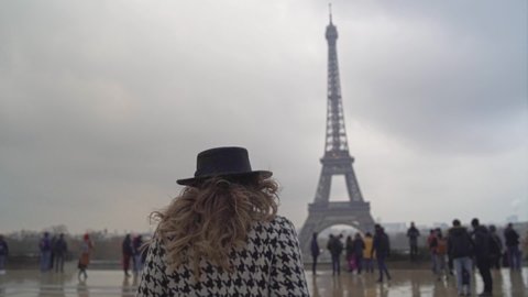 Young girl with long hair, red lipstick, glasses and beret walking and smiling on the Eiffel tower background