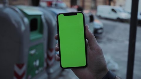 NEW YORK - April 19, 2019: Young hands using iPhone with vertical green screen on the back of the garbage containers 